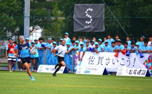 ラグビー成年男子決勝でトライを決める佐賀の福士萌起と佐賀応援団＝８日、SAGAサンライズパークボールフィールド